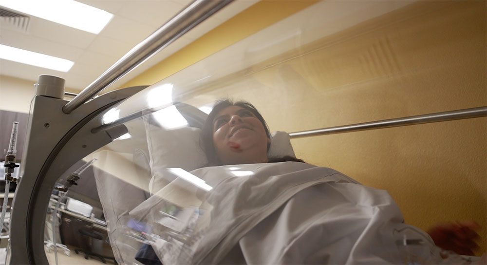 Una joven latina sonríe mientras descansa en una cámara de oxígeno hiperbárico