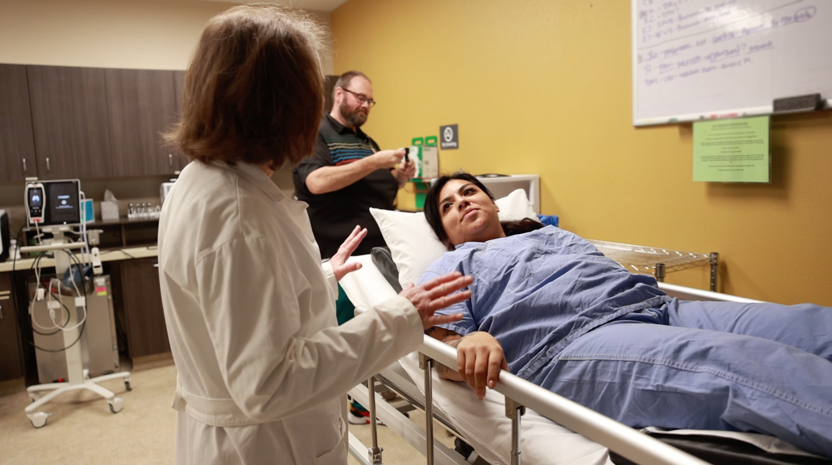 Una paciente en una cama de hospital mira a su médica, que la está preparando para el tratamiento con oxígeno hiperbárico.