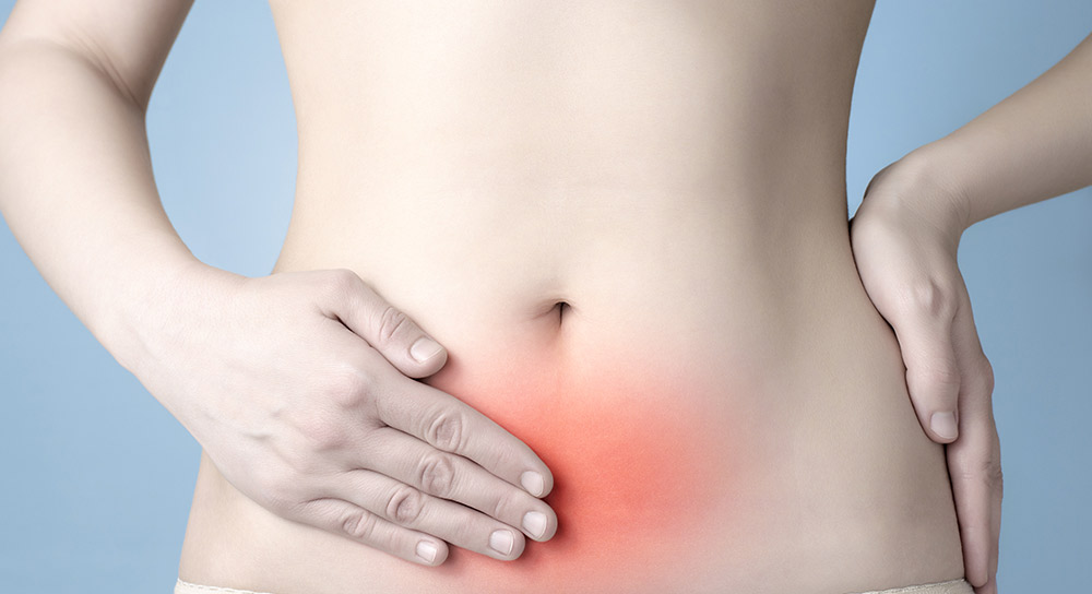 Close up of a woman's abdomen with a red area indicating pain. She has her hand placed over the area.