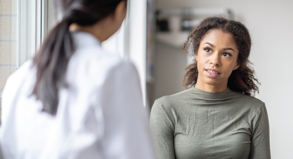 A young Black women pays attention to her doctor, an Asian woman with a ponytail