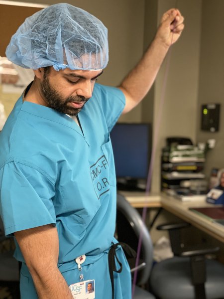 Dr. Khan in scrubs holds a long coil in one hand and pulls the length down
