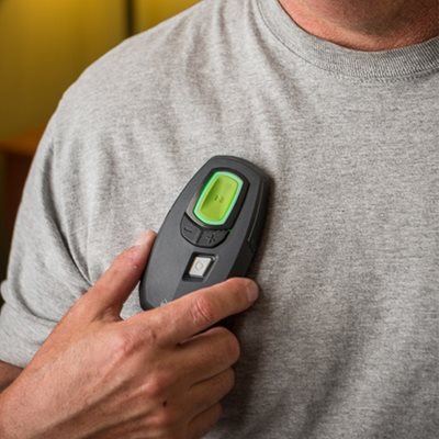 A close up of the Inspire device, which looks like a small remote control, is shown held next to a man's shirt.
