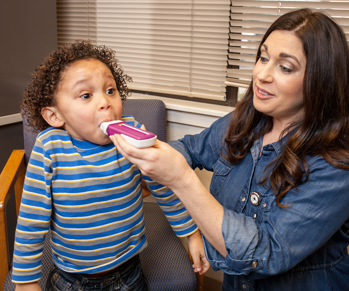 A care worker helps a toddler boy use an inhaler