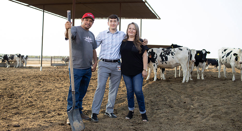Abraham stands proudly between his mom and dad in front of a group of dairy cows