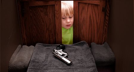 A young white kid with blond hair opens a wardrobe and reaches for a handgun inside