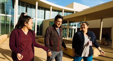 three Community healthcare workers, one man and two women, laugh and talk as they walk outside in front of a hospital