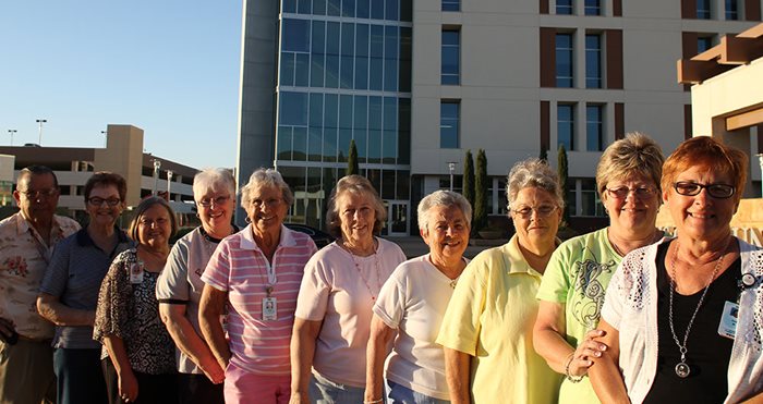 a line of people, the Clovis Community Guild, stands outside in front of a tall building