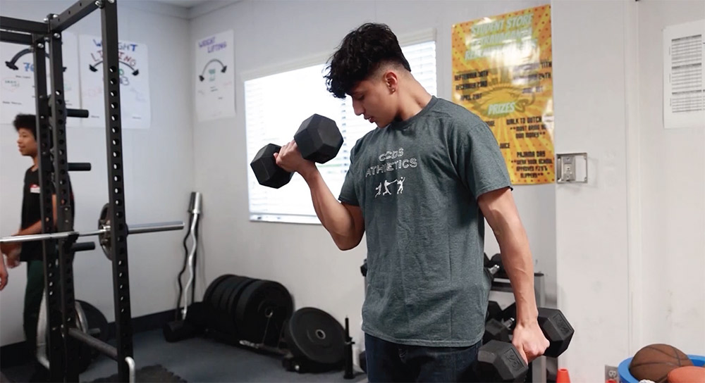A male high school student lifts weights in the gym of his school.