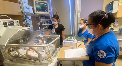Three student nurses gather around a NICU patient