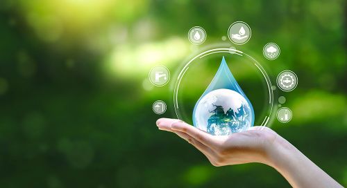 A white hand with palm up in front of a green forest background. Hovering above the hand is a large water drop with circles around it and the earth in the middle.