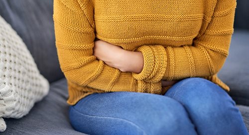 cropped image of a white woman in a yellow sweater and jeans holding her abdomen in apparent pan.