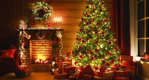 A living room scene with lighted Christmas tree, candles, and fireplace