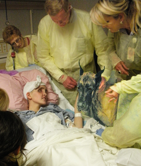 Shaela lays in her hospital bed with family and her Great Dane surrounding her