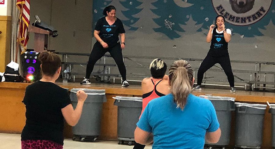 Two women on an elementary school stage lead a fitness class