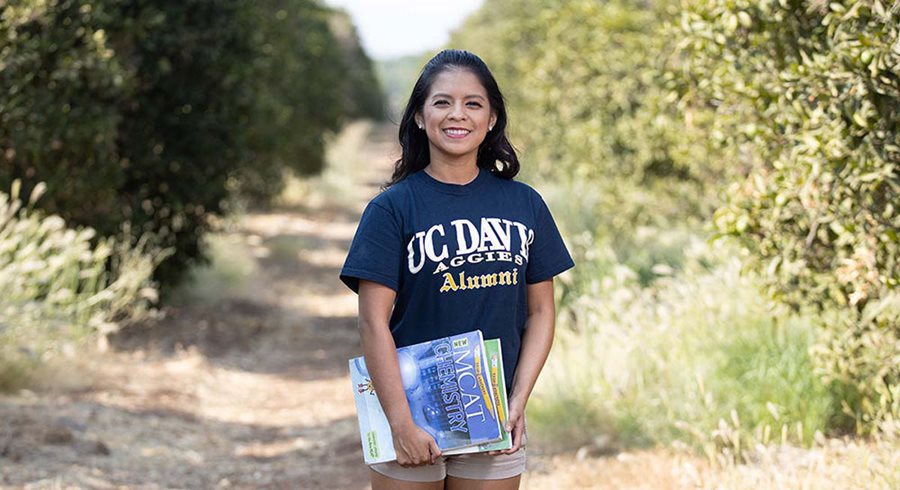 Jessica Camarillo stands in a fruit grove with her academic books