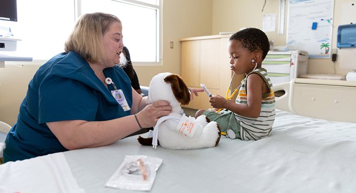 Child Life Specialist distracts a toddler with a stuffed animal and a stethoscope