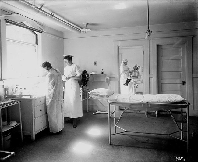 A black-and-white photo from inside the Burnett Sanitarium shows a doctor and two nurses tending to a sick child.